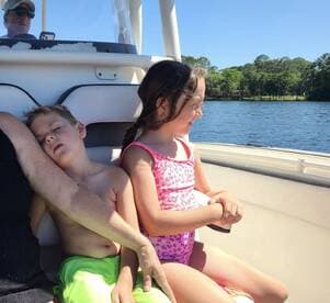 Two children enjoy a sunny day on a boat, with one resting while the other gazes at the water — a perfect family outing on the water.