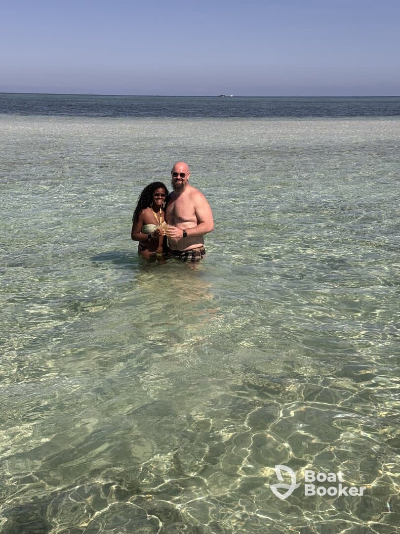 A couple enjoys a refreshing moment in the clear waters, celebrating with drinks — a perfect beach getaway experience.