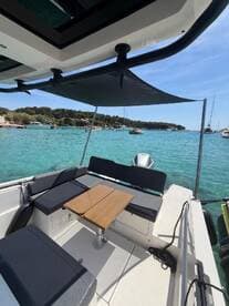 A cozy interior view of a boat's lounge area featuring comfortable seating and a table, perfect for relaxing while enjoying the scenic turquoise waters.