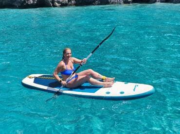 A woman enjoys paddleboarding in crystal-clear waters, showcasing the perfect blend of adventure and relaxation on the water.