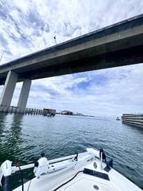 A view from the bow of a boat navigating under a bridge, showcasing the serene waters and cloudy sky — perfect for exploring coastal waterways.