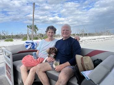 A couple enjoys a relaxing moment on a boat with their dog, surrounded by a scenic beach backdrop — perfect for a day of leisure on the water.
