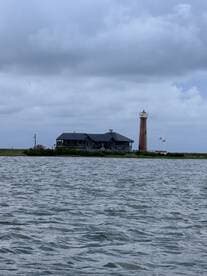 A scenic view of a lighthouse and a charming building along the shoreline, capturing the essence of coastal landmarks and tranquil waters.