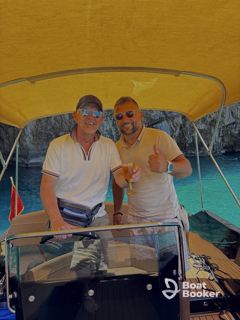 Two friends enjoy drinks aboard a boat, celebrating their time on the water with stunning turquoise views in the background.