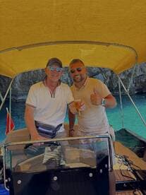 Two friends enjoy drinks aboard a boat, celebrating their time on the water with stunning turquoise views in the background.