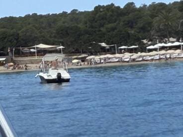 A boat approaches a lively beach scene, where guests enjoy the sun and relaxation — a perfect summer getaway.