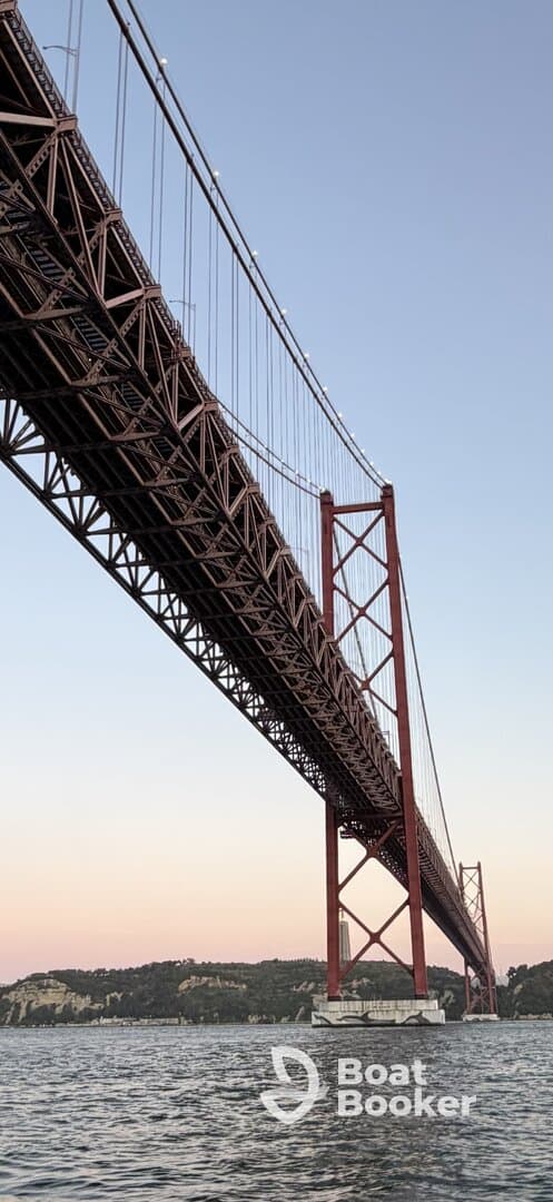 A view of a large bridge over water, capturing its architectural details against a pastel sky. The image does not clearly depict any boating activity or people.