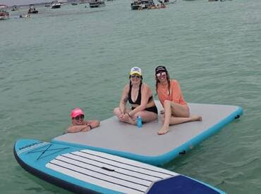 A fun group of friends relaxes on a floating mat in clear waters, enjoying a perfect summer day on the water.