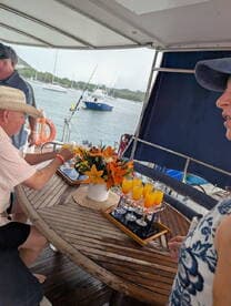 Guests enjoy a beautifully arranged table with cocktails and flowers aboard a boat, perfect for a relaxing day on the water.