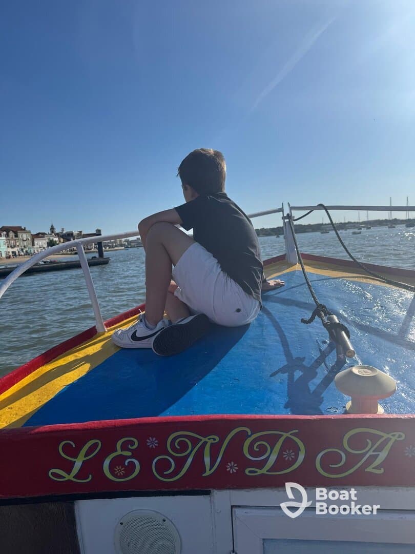 A young boy sits on the bow of a boat, gazing out at the water, capturing the essence of adventure and exploration on a sunny day.