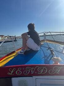 A young boy sits on the bow of a boat, gazing out at the water, capturing the essence of adventure and exploration on a sunny day.