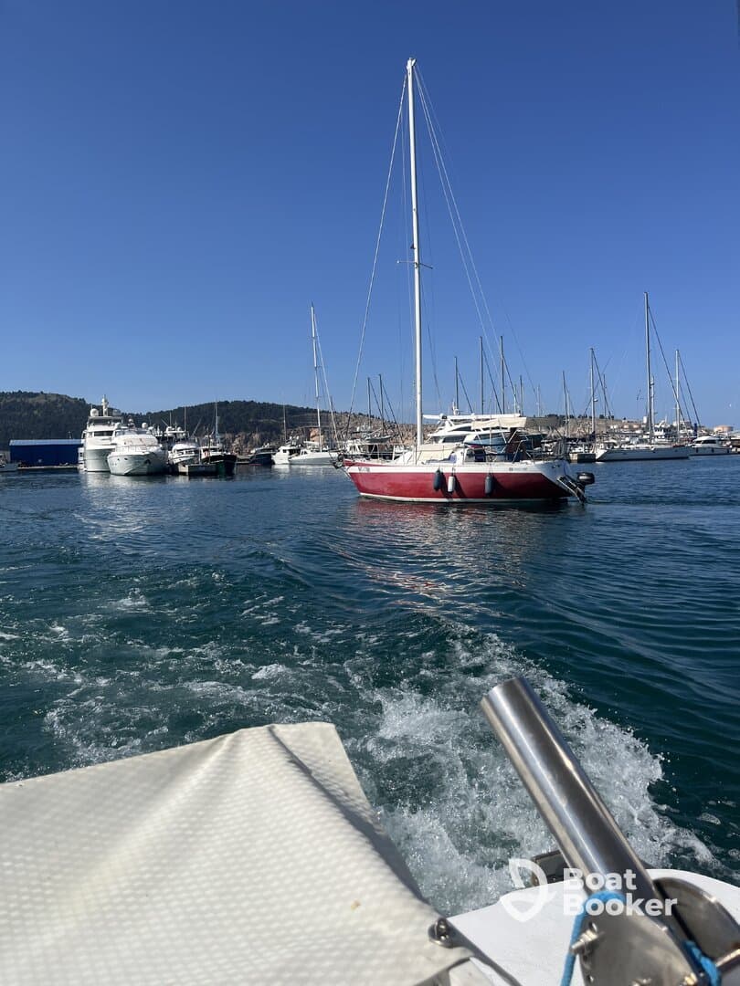 A picturesque view of a sailboat navigating through a marina, surrounded by various yachts under a clear blue sky.