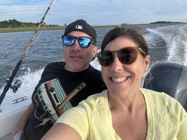 A cheerful couple enjoys a fishing trip on a boat, capturing a memorable moment with smiles and scenic views in the background.