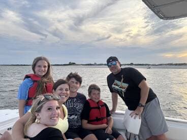 A joyful family poses together on a boat, enjoying their time on the water as the sun sets in the background — perfect for memorable family outings.