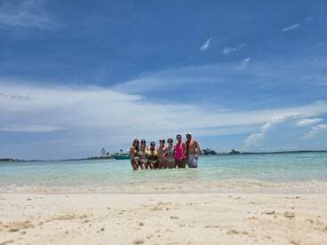 A lively group enjoys a sunny day at the beach, wading in the shallow waters and celebrating together — perfect for summer fun and memorable outings.