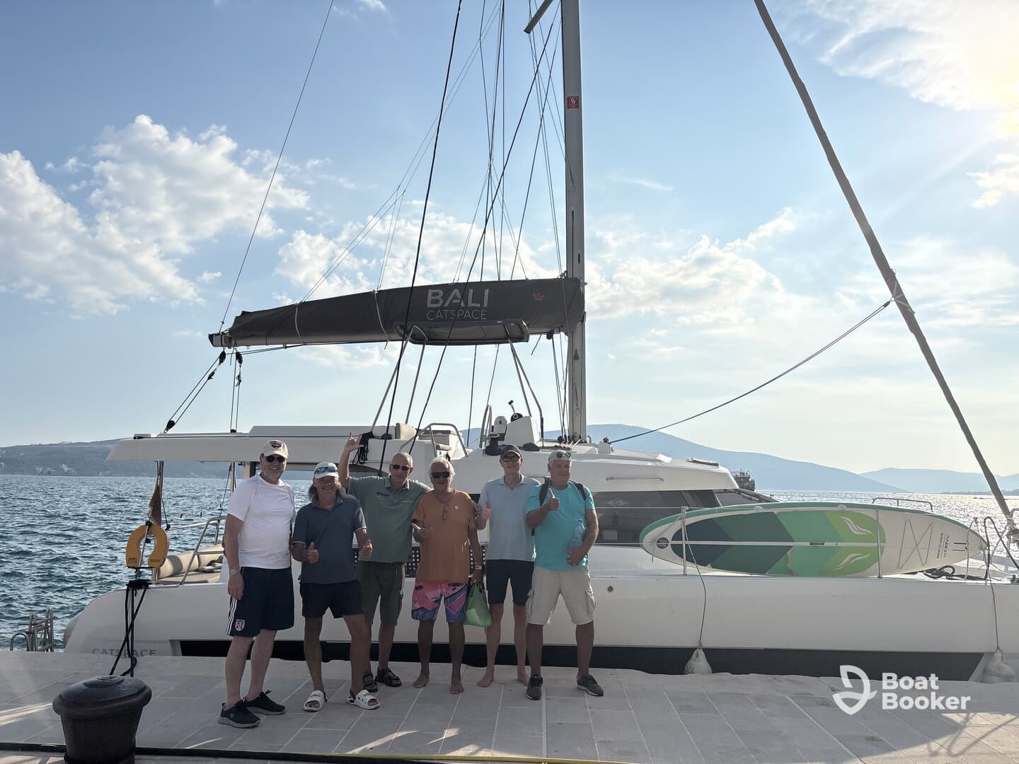 A cheerful group poses in front of a Bali Catspace catamaran, celebrating their boating adventure — perfect for group outings and memorable experiences on the water.