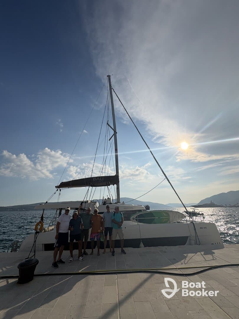 A group of friends poses in front of a catamaran at sunset, capturing a memorable moment before their sailing adventure.