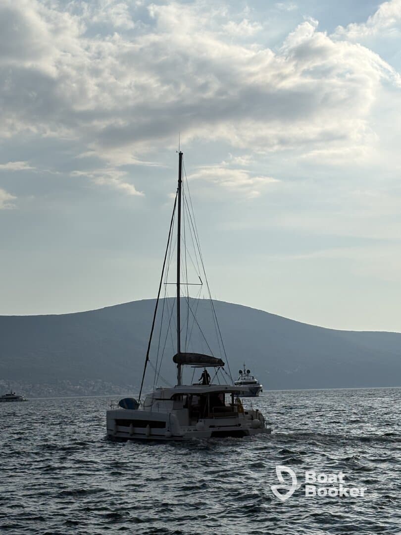 A catamaran sails through calm waters with a scenic backdrop of hills, showcasing the beauty of boating adventures.