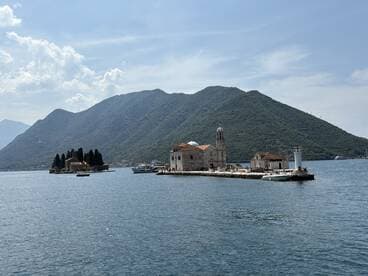 A picturesque view of an island with historic buildings set against a stunning mountainous backdrop, perfect for exploring coastal landmarks and enjoying scenic boat tours.