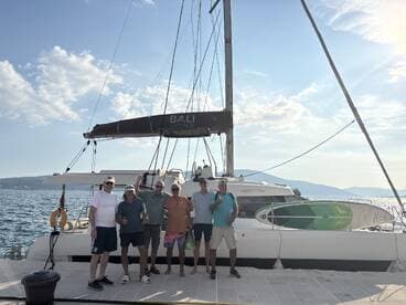 A cheerful group poses in front of a Bali Catspace catamaran, celebrating their boating adventure — perfect for group outings and memorable experiences on the water.