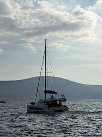 A catamaran sails through calm waters with a scenic backdrop of hills, showcasing the beauty of boating adventures.