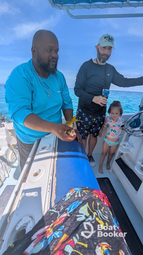 A family enjoys a fishing experience on a boat, with a child observing as an adult holds up a catch — a memorable day on the water.