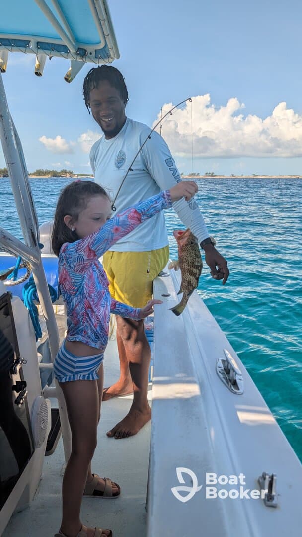 A young girl proudly holds up her catch while fishing with an adult on a boat, showcasing a joyful moment on the water.