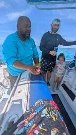 A family enjoys a fishing experience on a boat, with a child observing as an adult holds up a catch — a memorable day on the water.