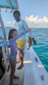 A young girl proudly holds up her catch while fishing with an adult on a boat, showcasing a joyful moment on the water.