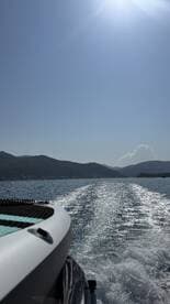 A sleek speedboat cuts through the shimmering waters, leaving a wake behind as it navigates the scenic coastline under a clear blue sky.