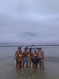 A fun group of friends enjoys a day at the beach, wading in shallow water with a boat anchored nearby — perfect for memorable summer outings.