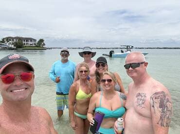 A cheerful group enjoys a day at the beach, posing for a selfie with a boat in the background — perfect for summer fun and memorable outings on the water.