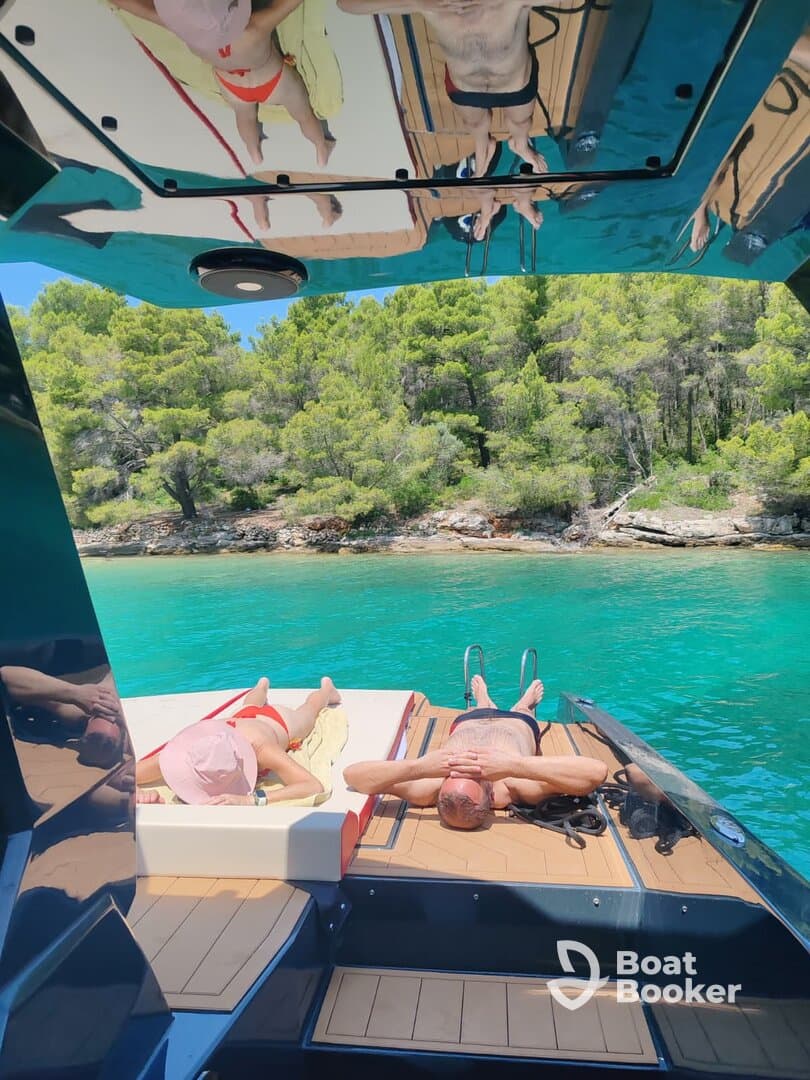 A couple enjoys a relaxing day on a boat, sunbathing on the deck surrounded by stunning turquoise waters and lush greenery — the perfect getaway for sun and sea lovers.