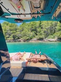 A couple enjoys a relaxing day on a boat, sunbathing on the deck surrounded by stunning turquoise waters and lush greenery — the perfect getaway for sun and sea lovers.