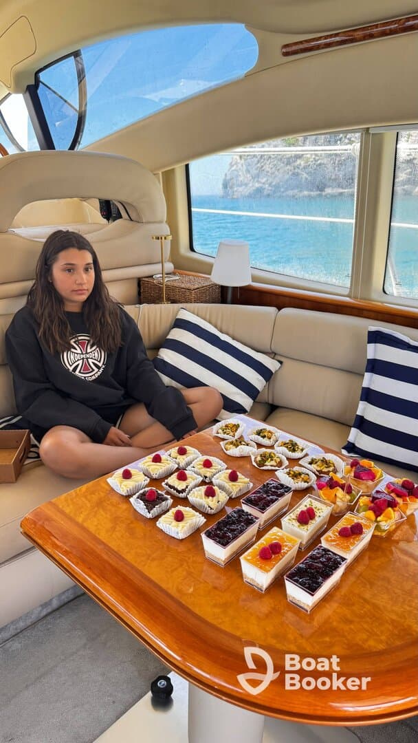 A young girl sits on a plush boat interior, surrounded by an array of delicious desserts, perfect for a sweet treat while enjoying a day on the water.
