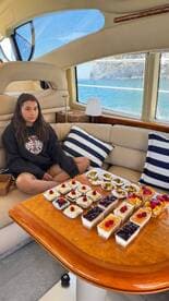 A young girl sits on a plush boat interior, surrounded by an array of delicious desserts, perfect for a sweet treat while enjoying a day on the water.