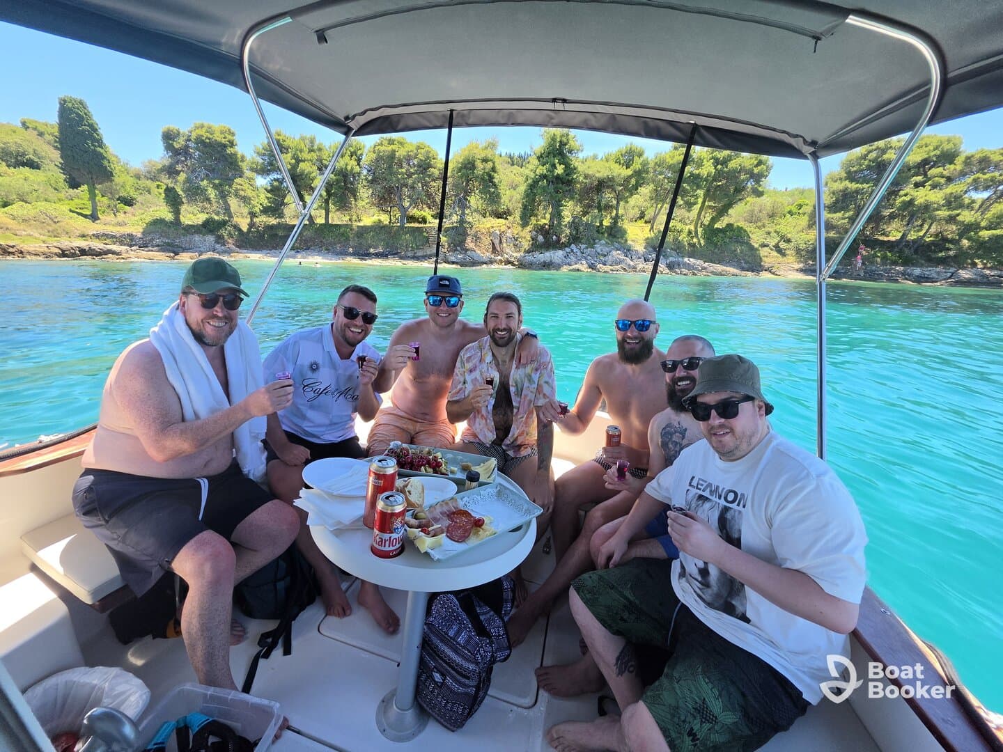 A lively group of friends enjoys a fun day on the water, celebrating with food and drinks aboard a boat, surrounded by stunning turquoise waters.