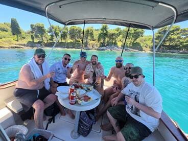 A lively group of friends enjoys a fun day on the water, celebrating with food and drinks aboard a boat, surrounded by stunning turquoise waters.