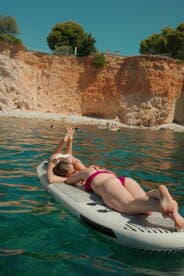 Two friends relax on a paddleboard in crystal-clear waters, enjoying a sunny day at the beach — a perfect moment for summer fun and relaxation.