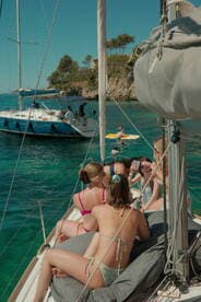A lively group enjoys drinks and sunbathing on the deck of a sailboat, creating unforgettable memories while sailing in beautiful waters.