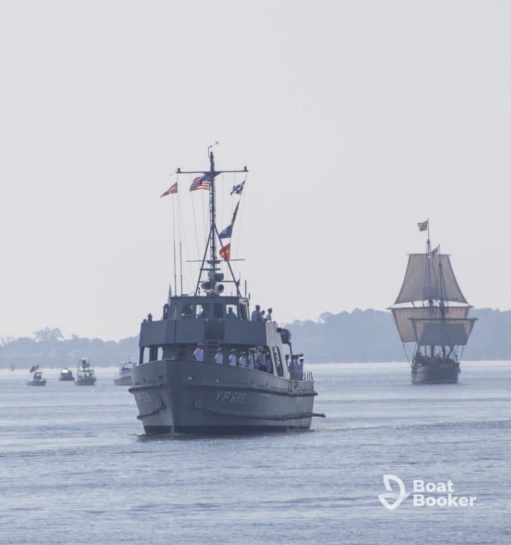 A naval vessel sails alongside a historic ship, showcasing a vibrant maritime scene with crew members visible on deck.