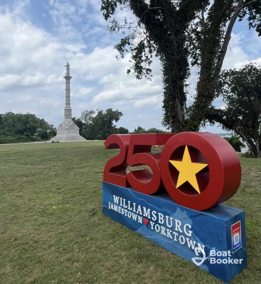 A scenic view featuring a commemorative sign for the 250th anniversary of Williamsburg, Jamestown, and Yorktown, with a monument in the background.