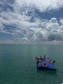 A lively group enjoys a day on a floating mat in clear turquoise waters, perfect for relaxation and fun under the sun.