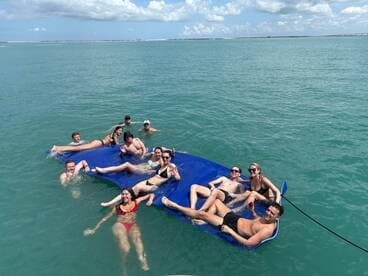 A lively group enjoys a sunny day on a floating mat in clear waters, perfect for fun and relaxation during their boating adventure.