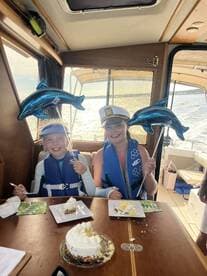 Two young girls celebrate with cake and dolphin balloons aboard a boat, capturing a joyful moment during their special occasion on the water.