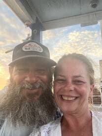 A joyful couple smiles for a selfie during a beautiful sunset, capturing a memorable moment on their boating adventure.