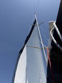 A close-up view of a sailboat's sail against a clear blue sky, showcasing the vessel's structure and design while underway.