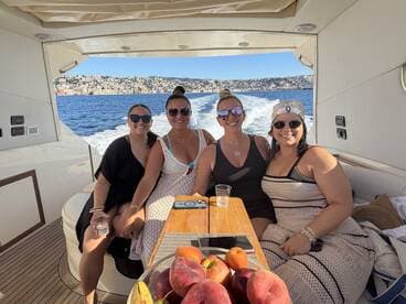A joyful group of friends enjoys a sunny day on a boat, celebrating with drinks and stunning views of the coastline — perfect for memorable outings on the water.