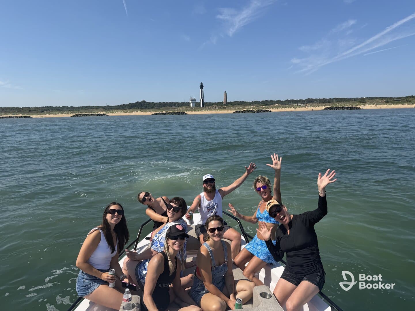 A lively group of friends enjoys a sunny day on the water, celebrating with drinks and smiles, with a picturesque lighthouse in the background.