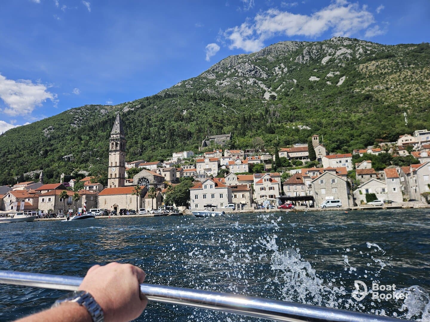 A scenic view of a charming coastal village with a historic church, captured from a boat, showcasing the stunning mountains and clear waters of the region.